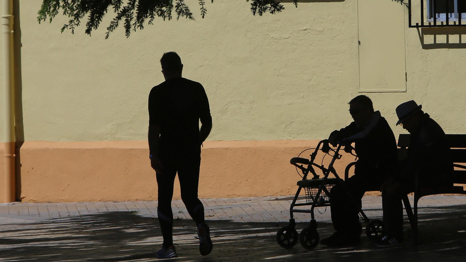 Dos personas mayores conversan sentados en un banco en un día soleado