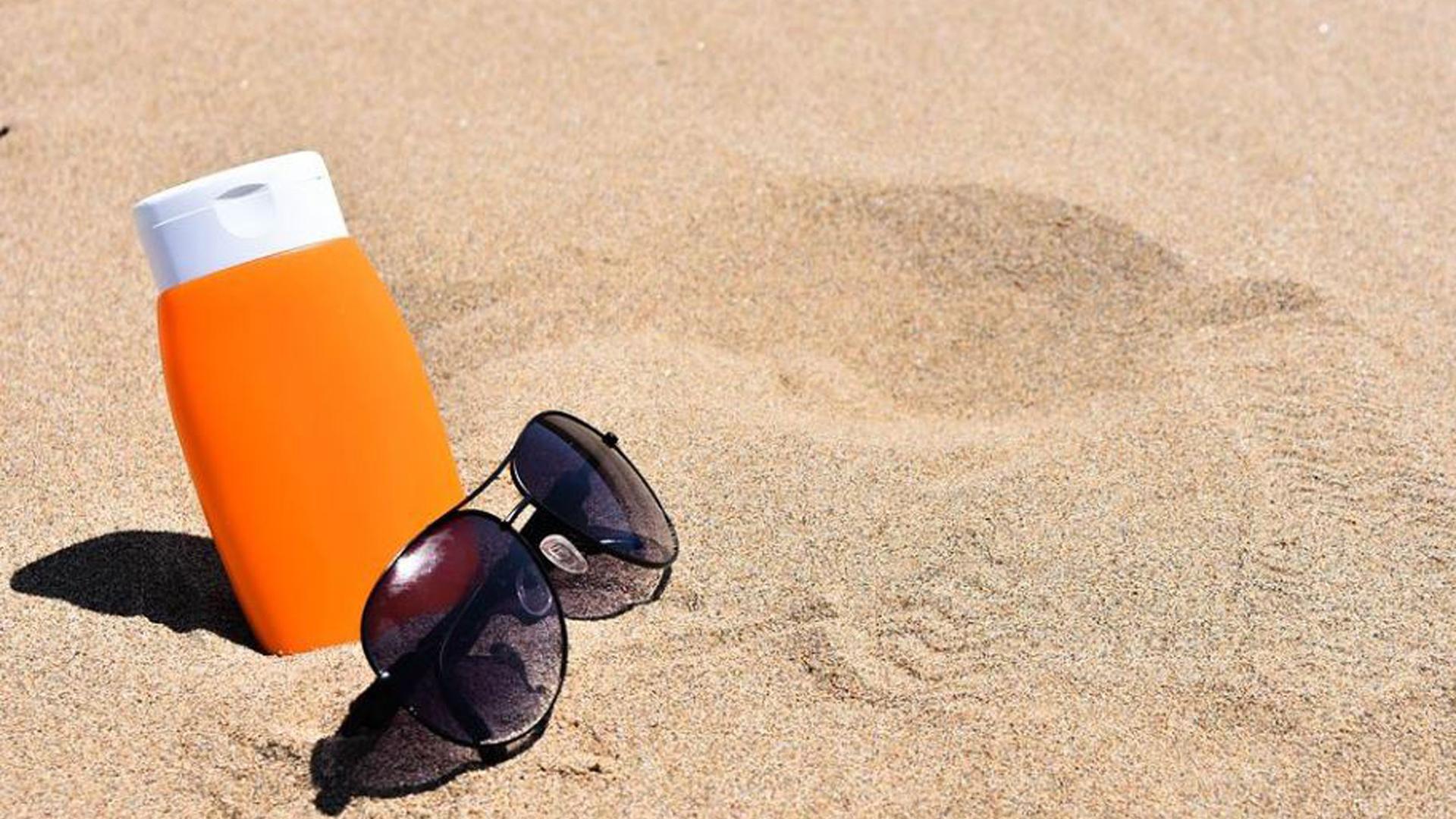 Unas gafas de sol y crema sobre la arena