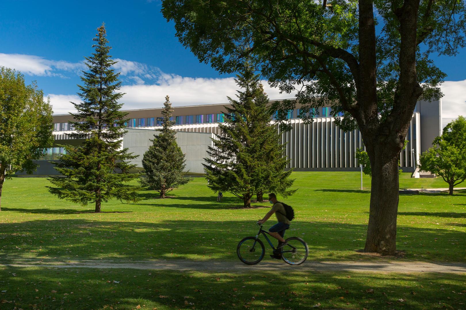 Un estudiante circula por el campus de la Universidad de Navarra con el edificio Amigos al fondo
