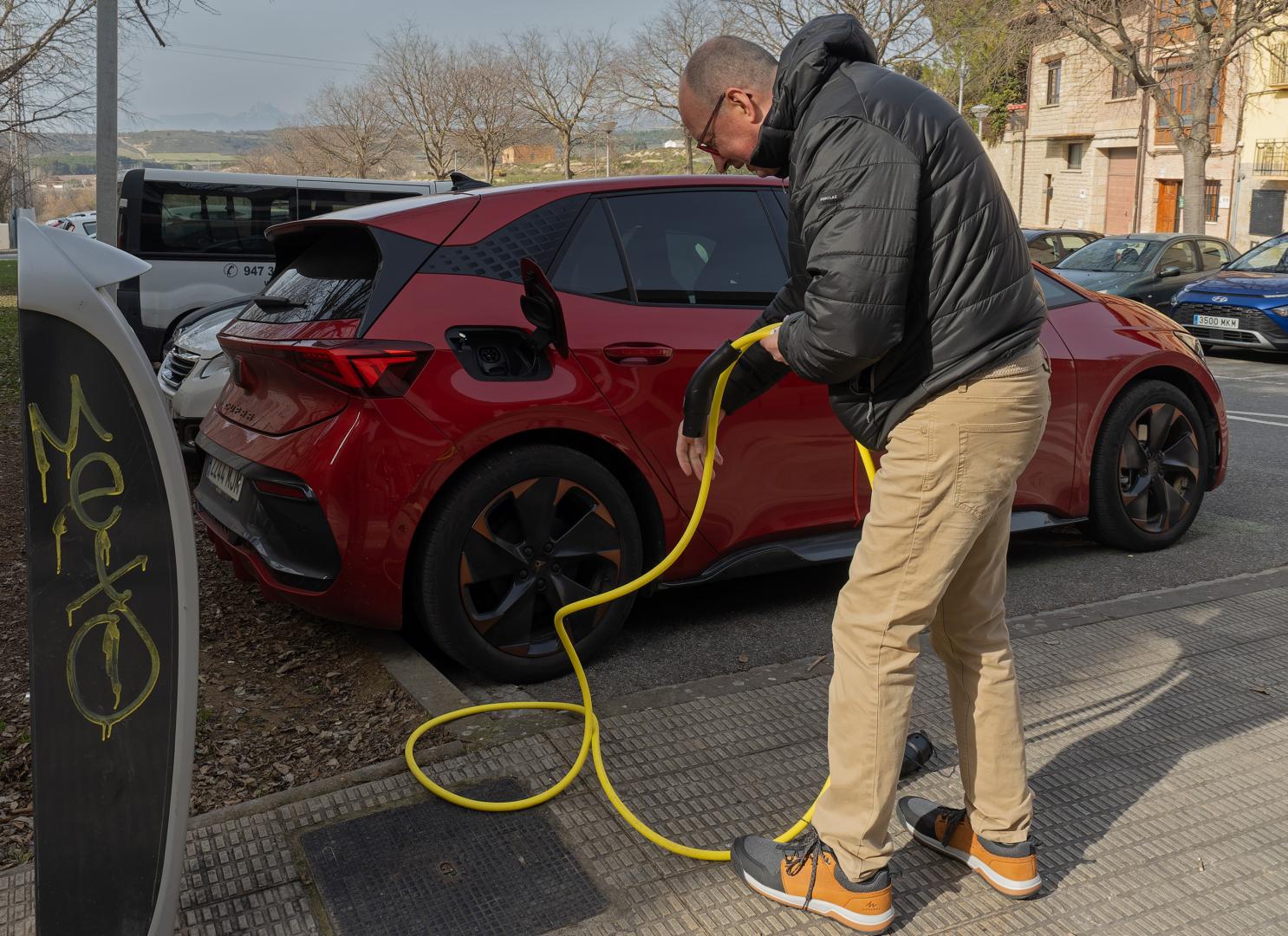 Un automovilista prepara el cable de recarga para enchufar un Cupra Born en una calle de Viana
