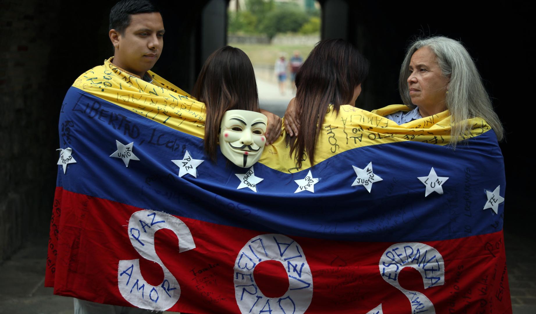 Ali Gómez, Eglee Torres y otras dos compatriotas, que prefieren no identificarse por temor a posibles represalias en su país, se envuelven en una bandera de hilo tejida en 2014 para manifestarse contra el régimen de Nicolás Maduro