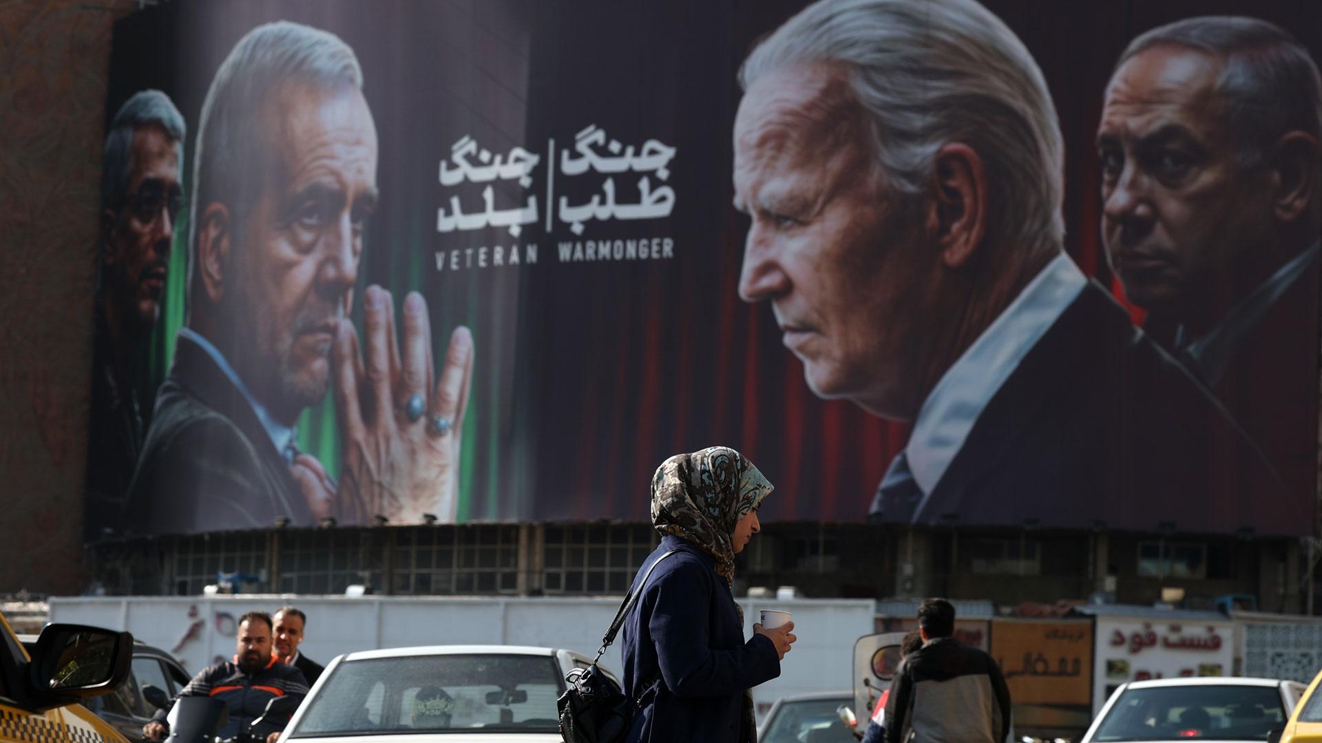 Los iraníes pasan junto a un cartel antiisraelí y estadounidense que muestra fotografías del presidente iraní Masoud Pezeshkian y el comandante militar del Cuerpo de la Guardia Revolucionaria Islámica iraní, General Mohammad Bagheri,frente al presidente estadounidense Joe Biden y el Primer Ministro de Israel, Benjamin Netanyahu