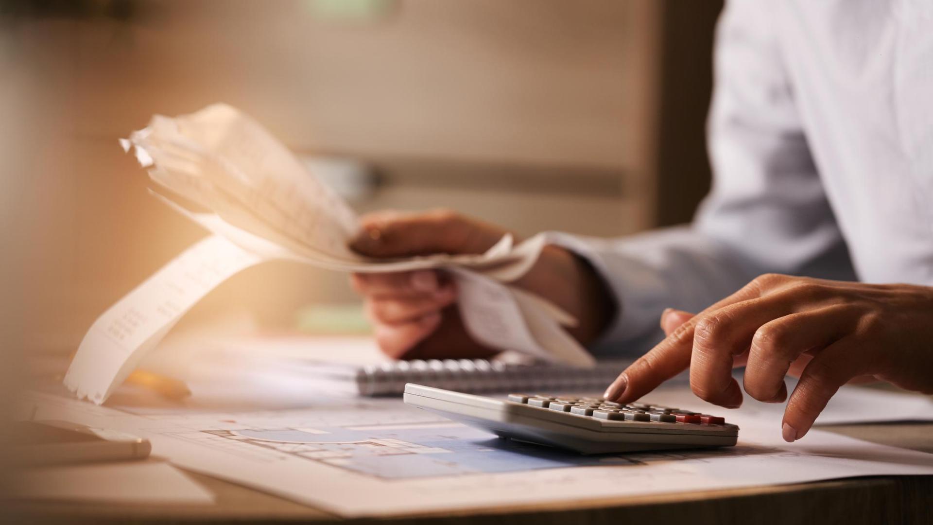 Primer plano de un economista que usa una calculadora mientras revisa las facturas y los impuestos en la oficina
