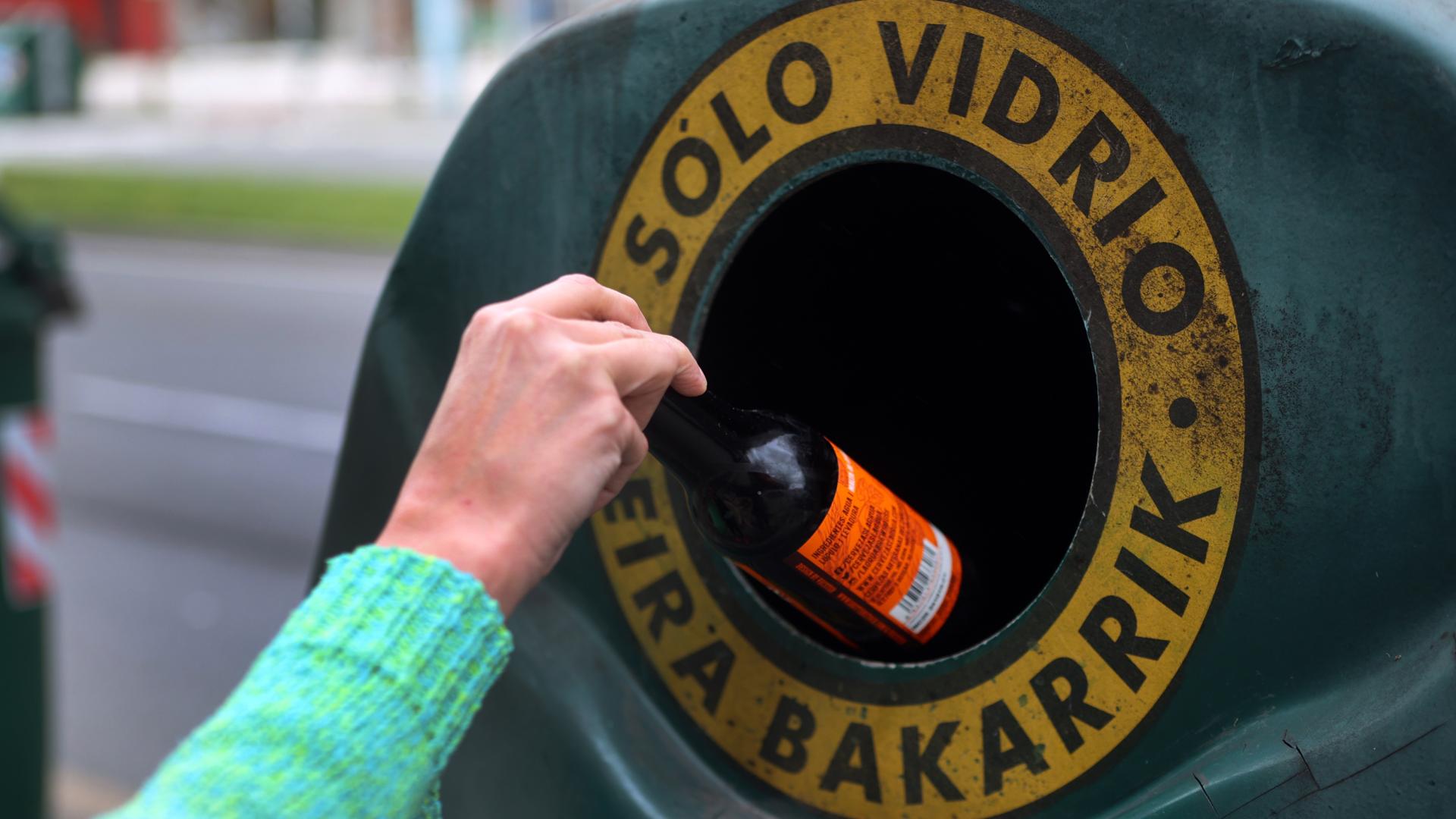 Una personas introduce una botella de cristal en un contenedor en Pamplona.