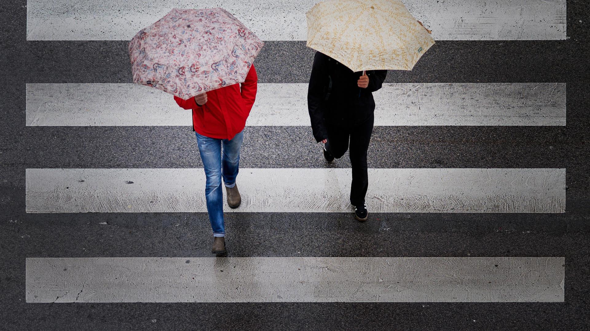 Dos peatones cruzan bajo sus paraguas un paso de peatones en Pamplona este martes.
