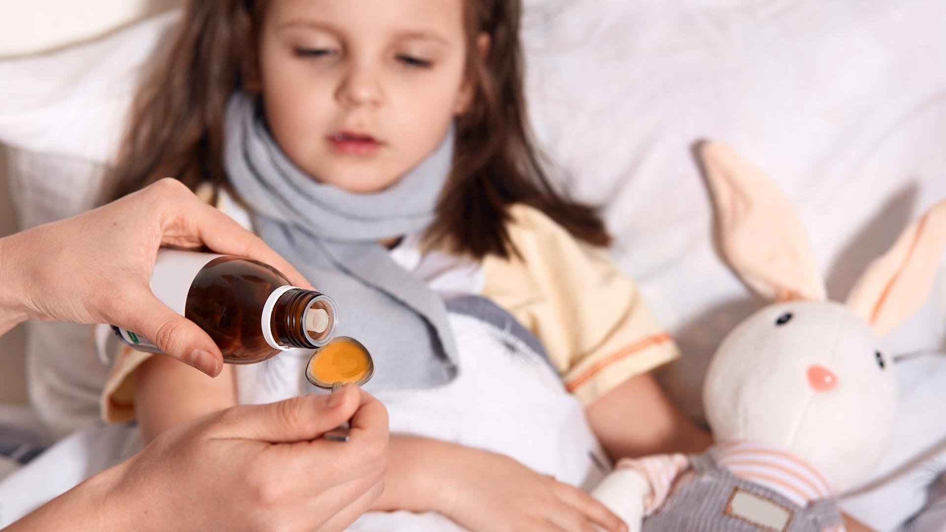Una persona administra jarabe a una niña
