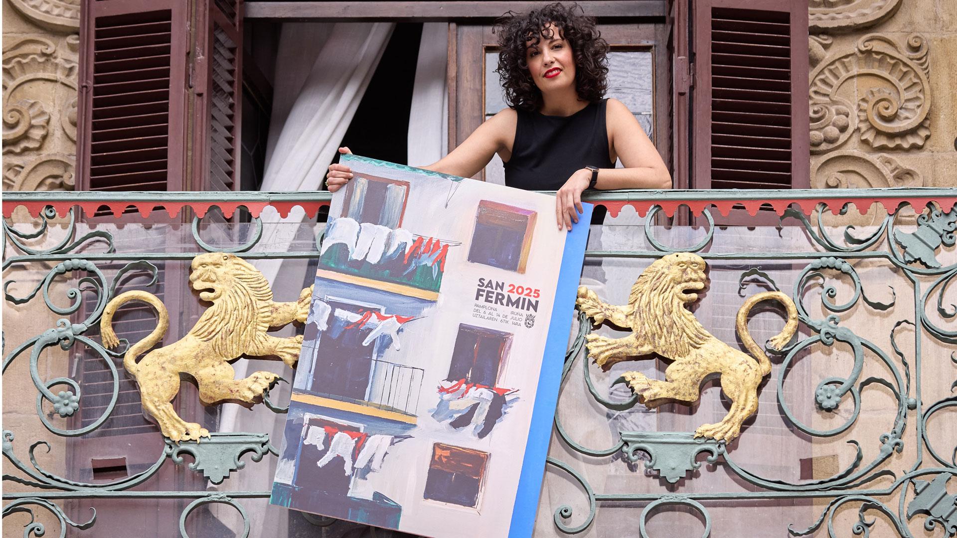 Sanda Nadal posa con el cartel ganador de San Fermín 2025, 'Hogar pamplonica', en el balcón del Ayuntamiento de Pamplona