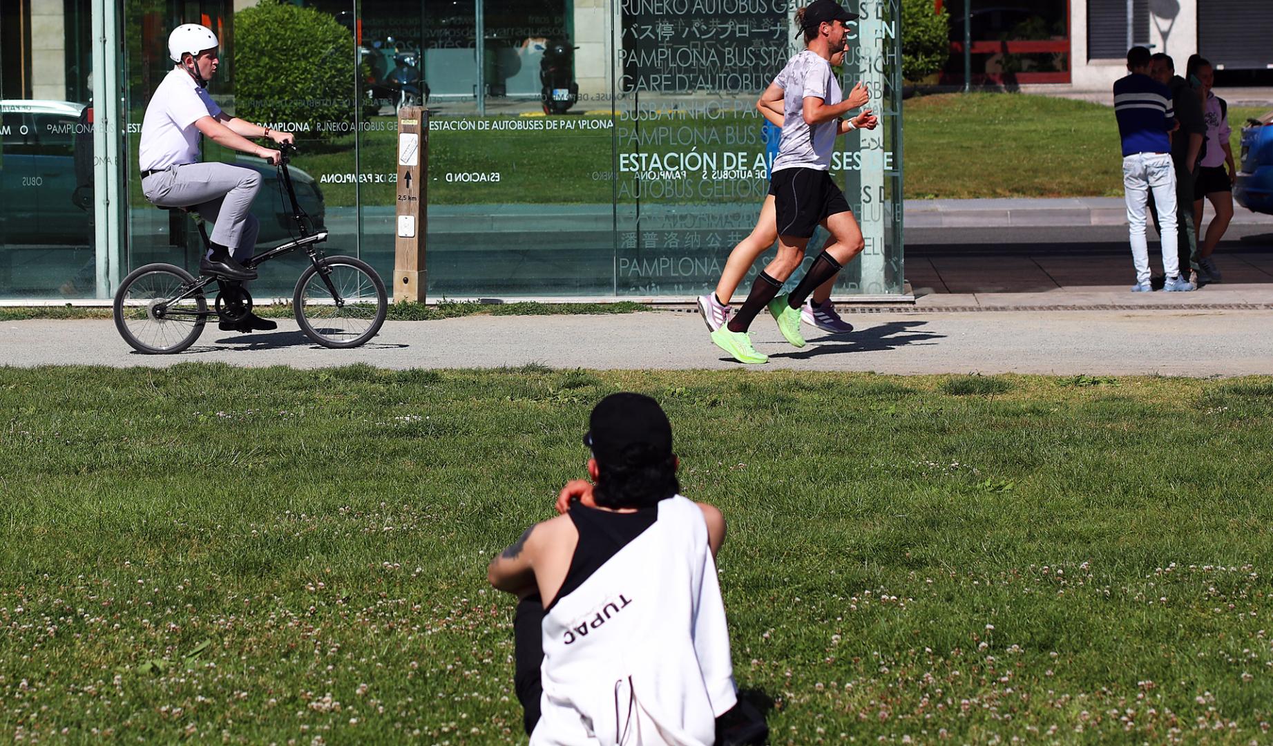 Una persona se sienta y observa pasar a otras en una tarde solada la Vuelta del castillo de Pamplona /
