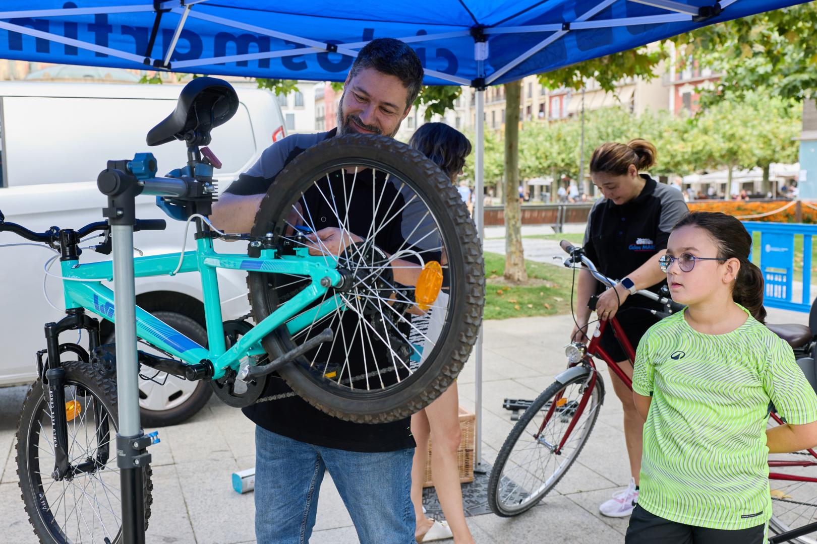 Un técnico de Ciclos Martín pone a punto la bici de una niña en la plaza del Castillo, dentro de la Semana de la Movilidad