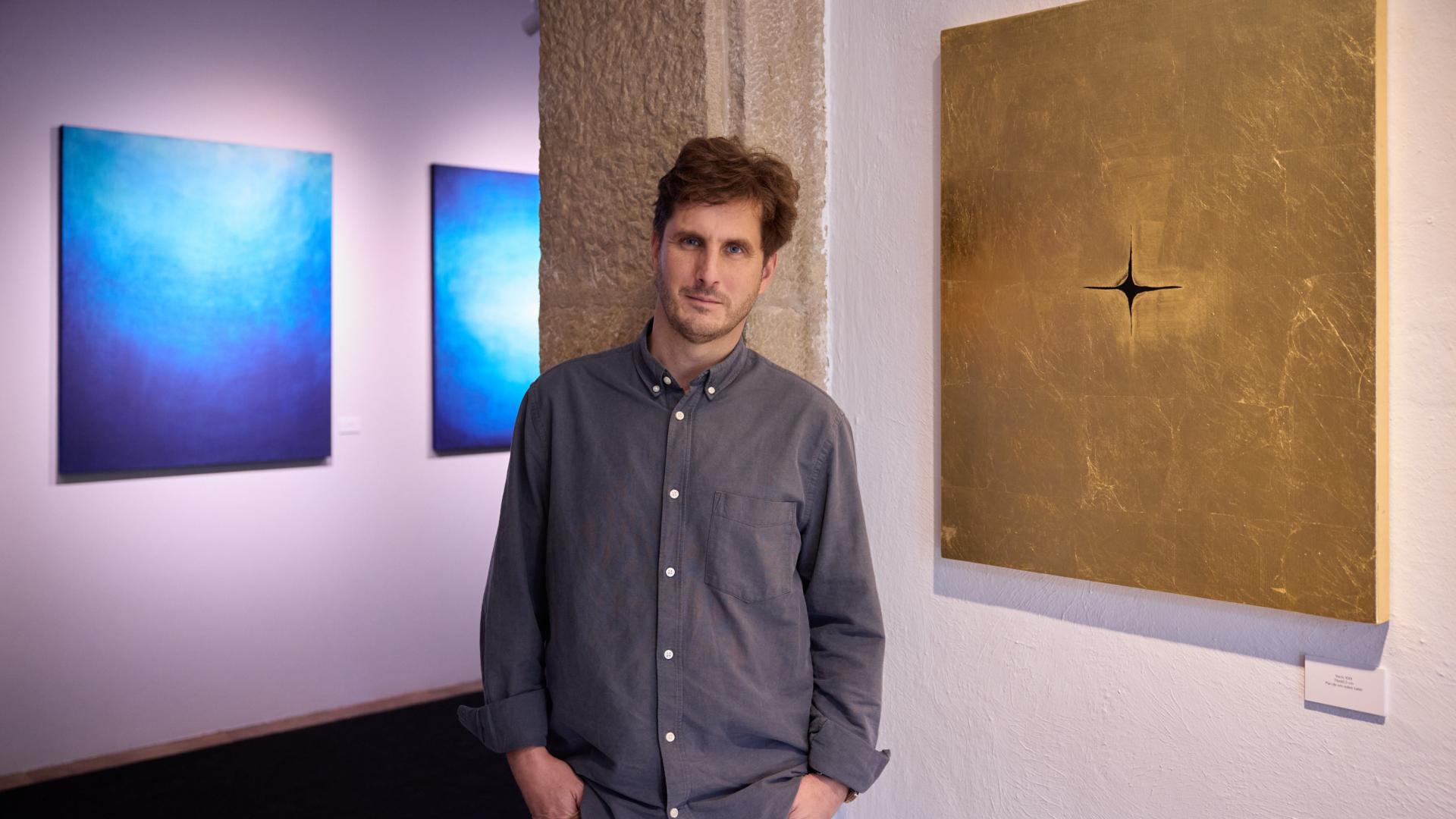 El artista Alberto Guerrero posa en La Puerta Gótica, entre las obras que componen la serie 'Vacío' (doradas) y las que componen la serie 'Misterio' (azules)