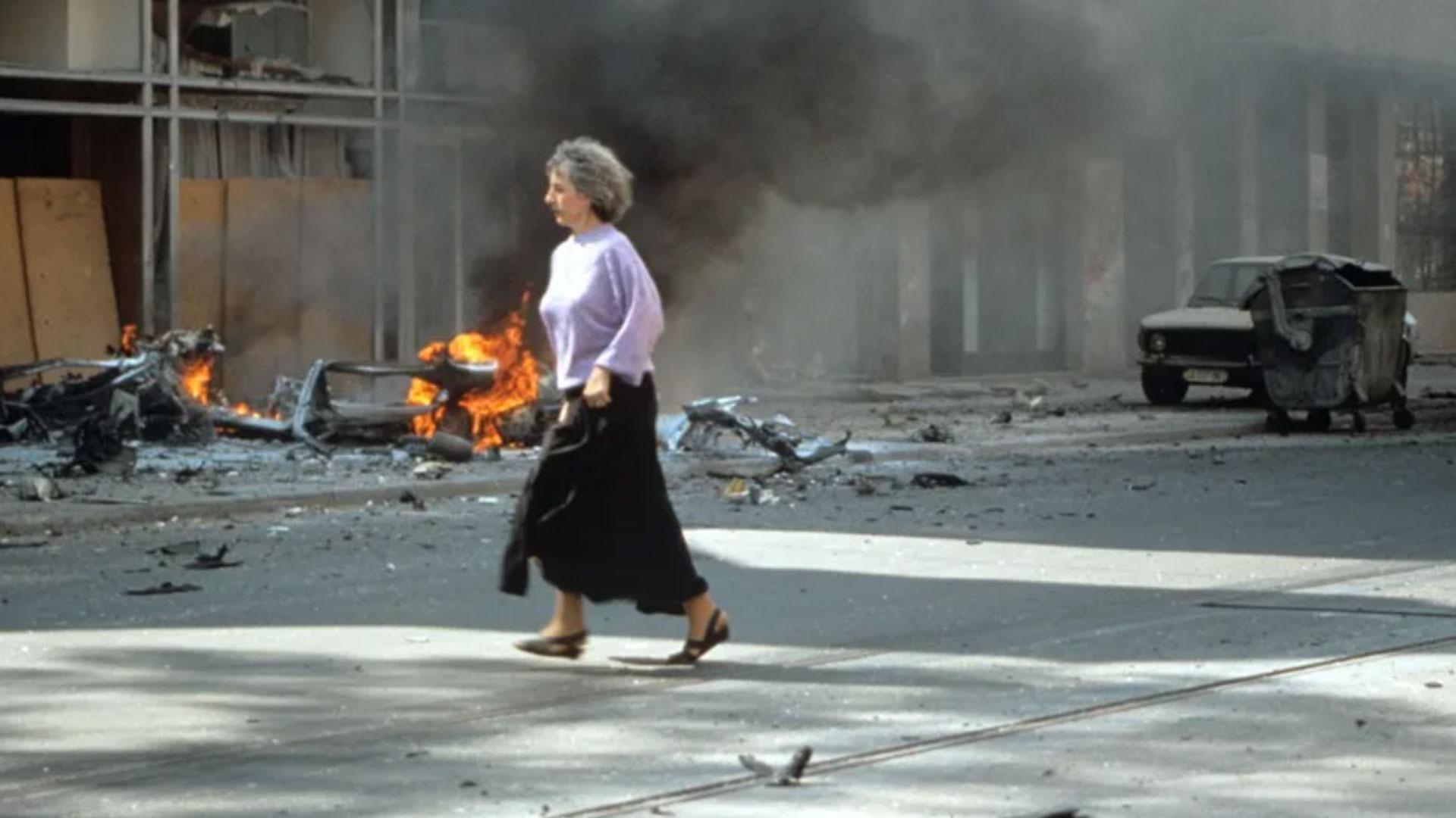 Una mujer corre ante un edificio bombardeado en Sarajevo