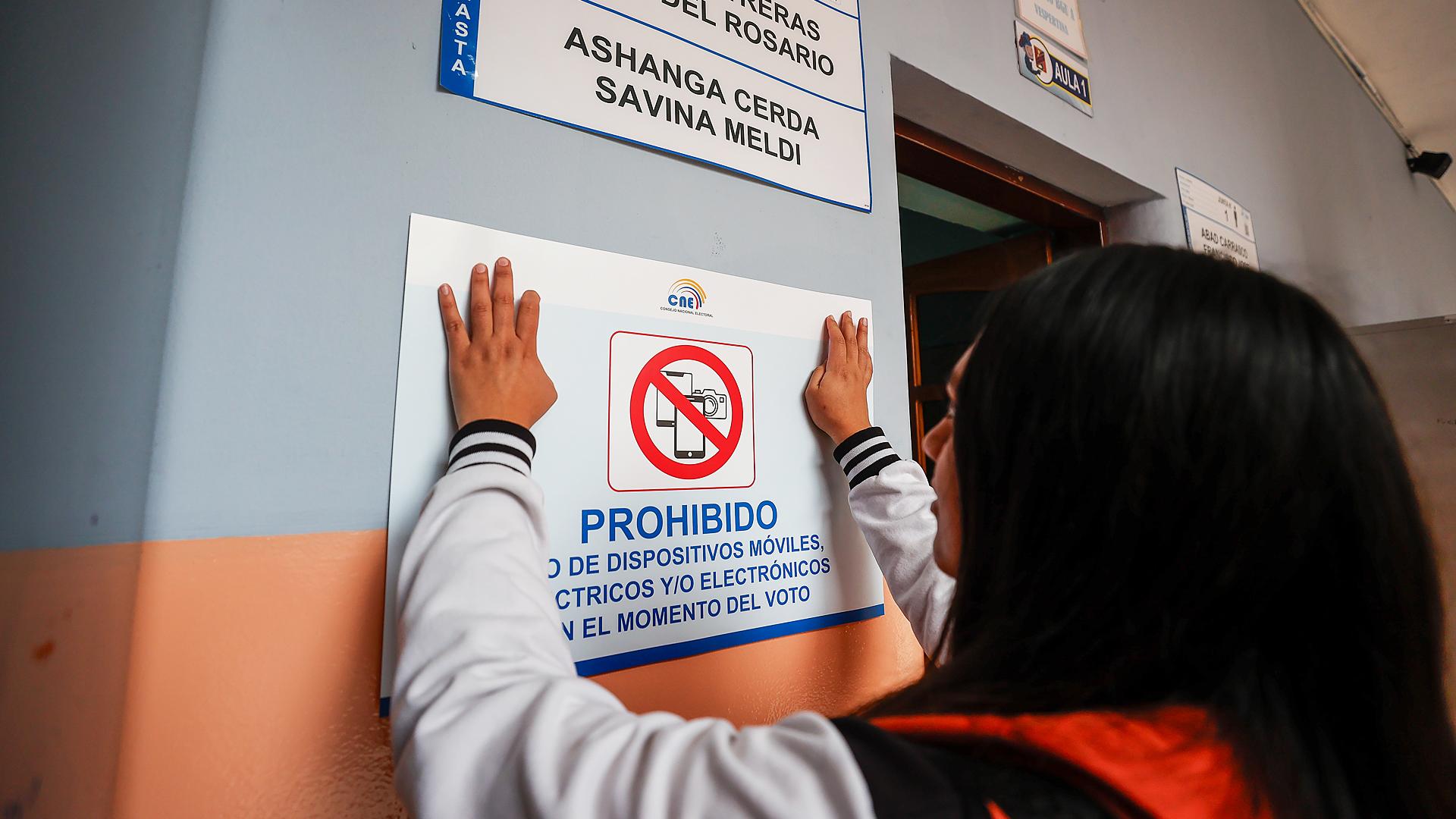 Una persona pega un aviso informativo en un puesto de votación a un día del referéndum en el colegio Benalcázar, en Quito (Ecuador) /