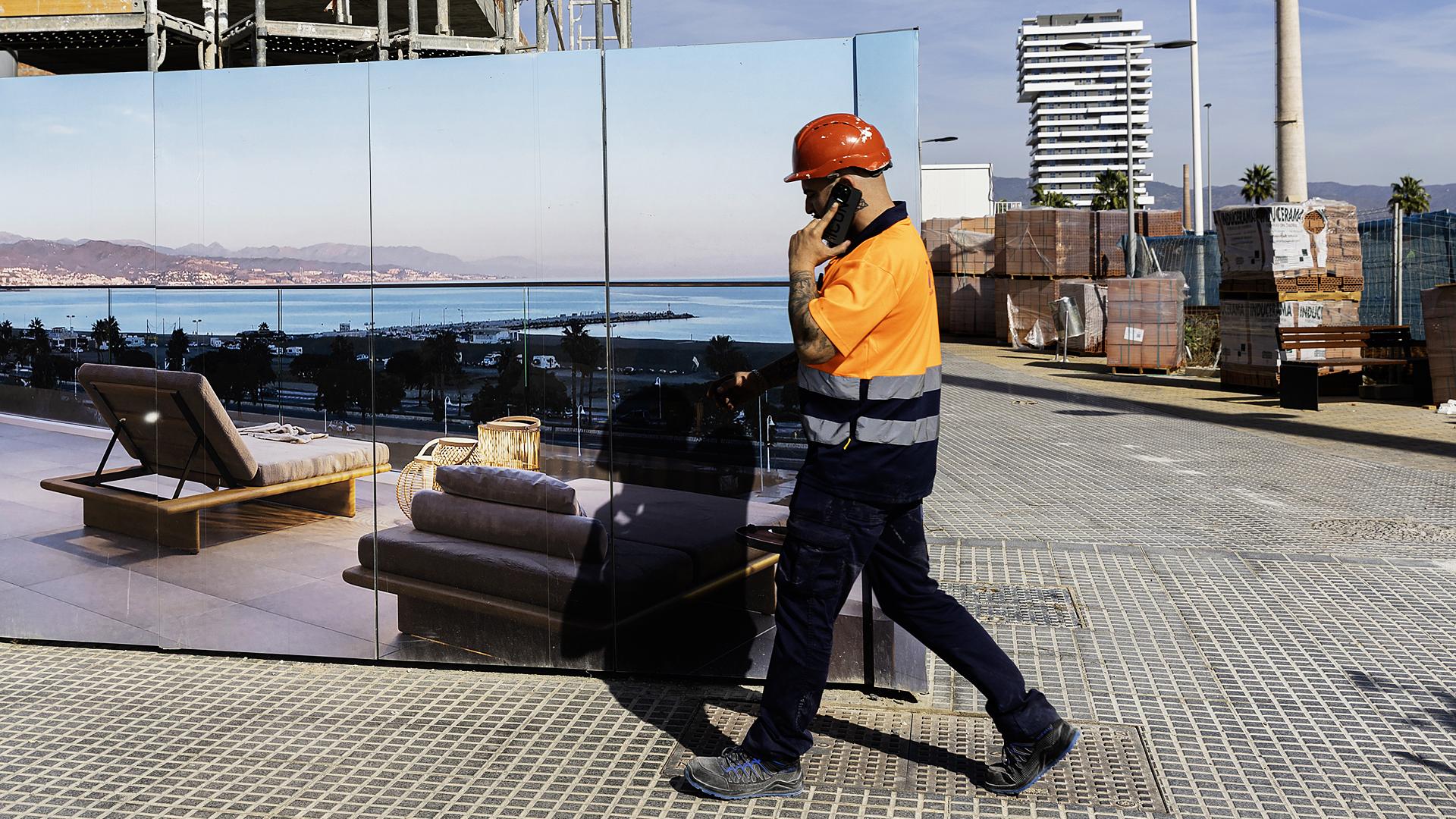 Un operario ante una publicidad de viviendas de lujos con las Torres de Málaga al fondo /