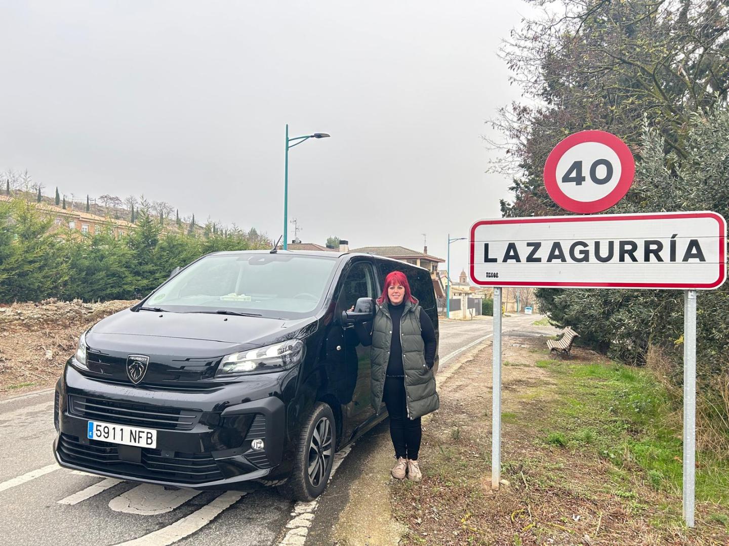 Blanca Baquedano Díaz, con su taxi y un cartel de su pueblo, Lazagurría.