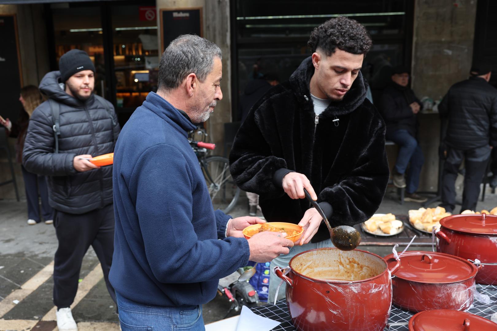Un voluntario sirve un plato de comida caliente a una persona, este 23 de diciembre en la plaza del Ayuntamiento de Pamplona.