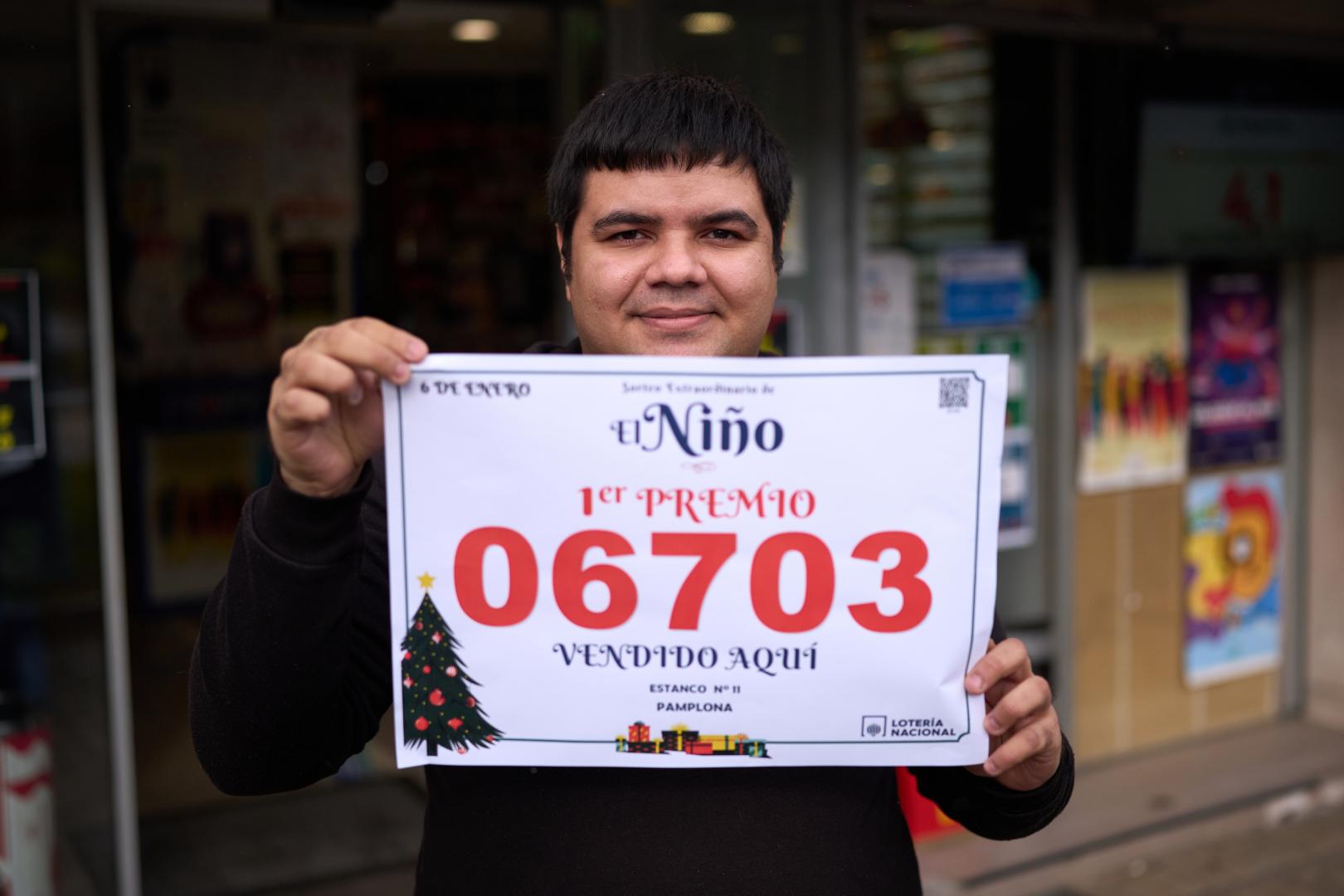 Andrey Mendes muestra con orgullo el cartel con el número agraciado delante de la administración de loterías en el número 52 de la avenida de Barañáin