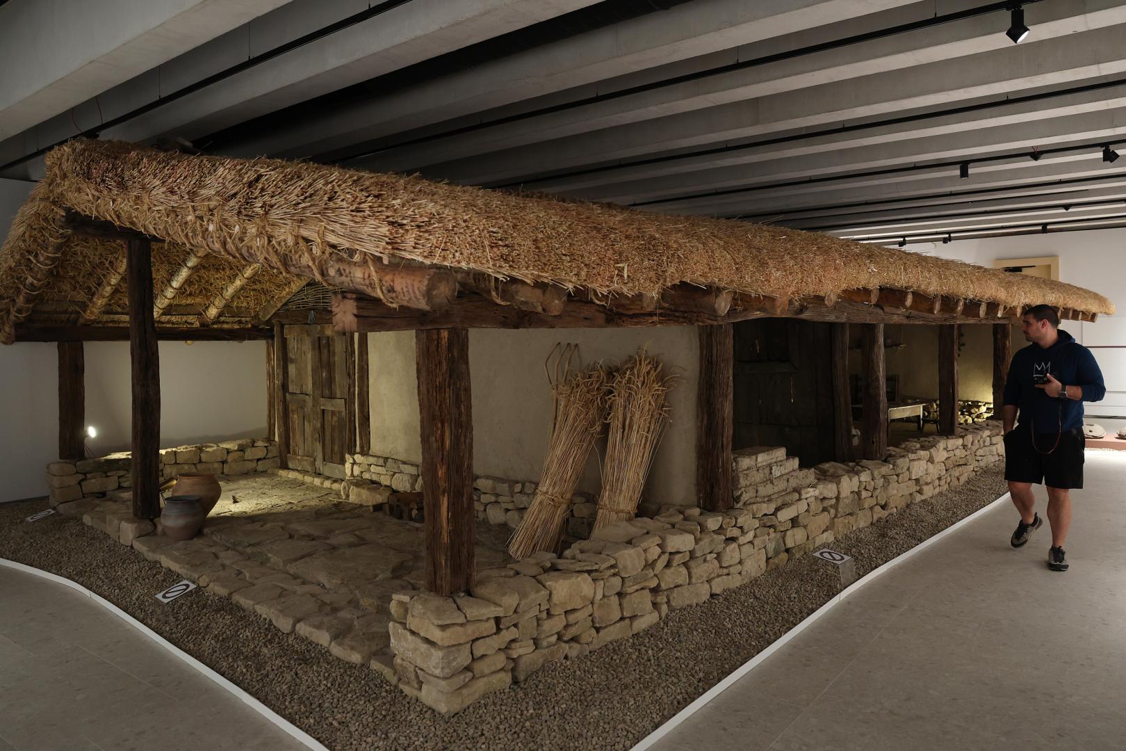 Un visitante observa la reconstrucción, a escala real, de la vivienda donde se halló la Mano de Irulegi. En el dintel  de la puerta de la casa (izq.) se ha colocado una réplica de la Mano.