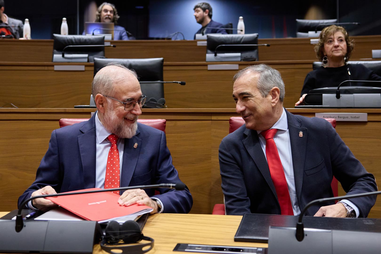 Los consejeros de Salud, Fernando Domínguez, y de Cohesión Territorial, Óscar Chivite, conversan en el hemiciclo del Parlamento