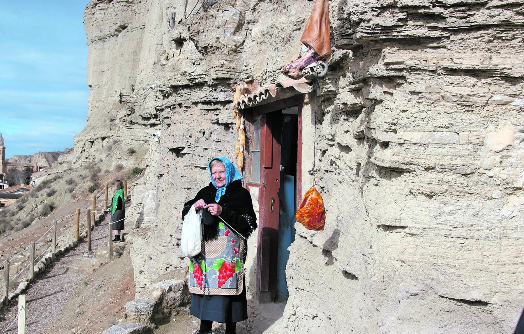 Una mujer tejiendo en la entrada de una de las siete viviendas que se han rehabilitado