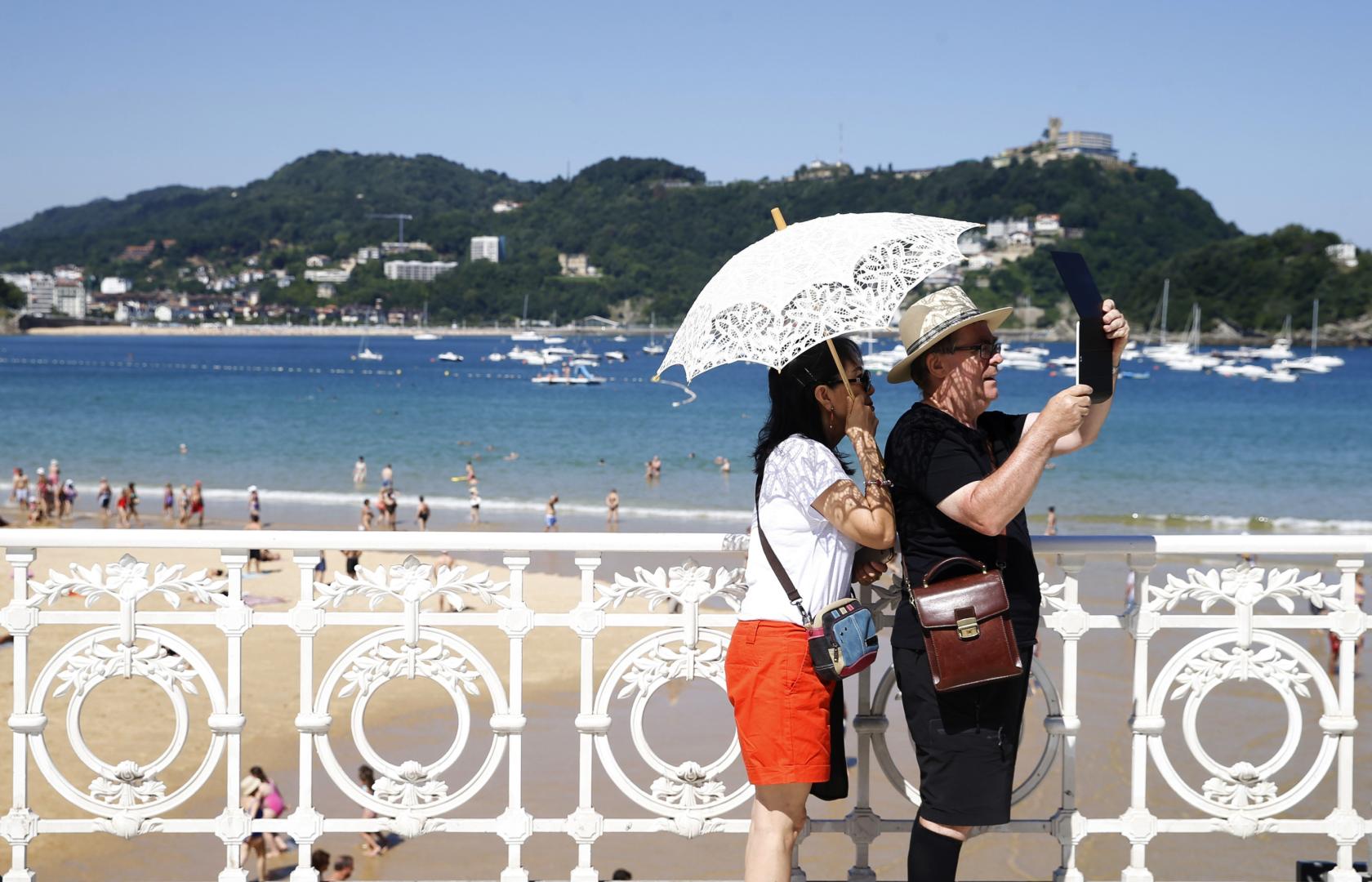 En una imagen de archivo, Una pareja de turistas se protege del sol junto a la playa de La Concha de San Sebastián.