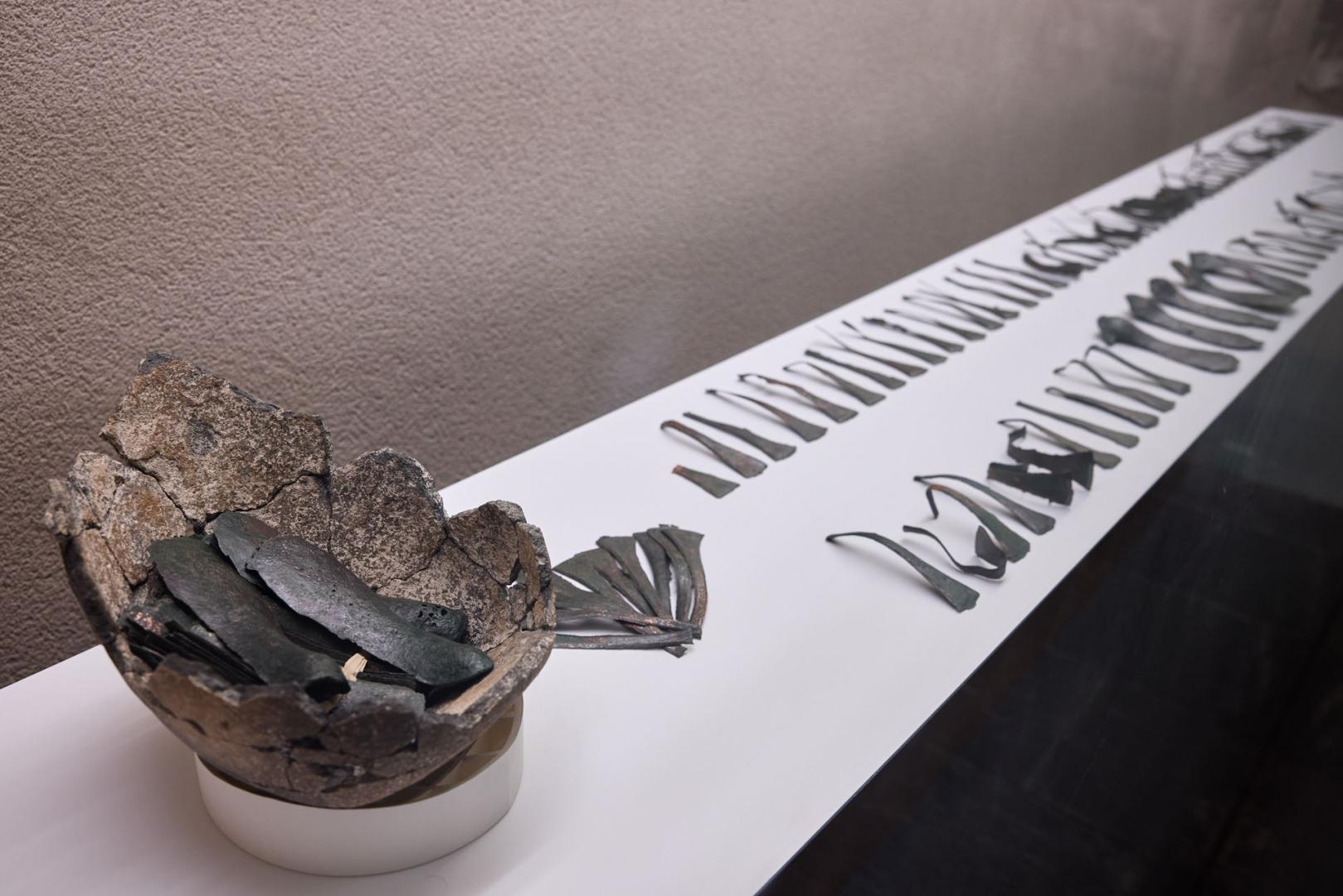 La vitrina con las piezas de bronce halladas en el yacimiento de Tafalla. A la izquierda, la vasija donde estaban guardadas, con los lingotes agrupados de diez en diez.