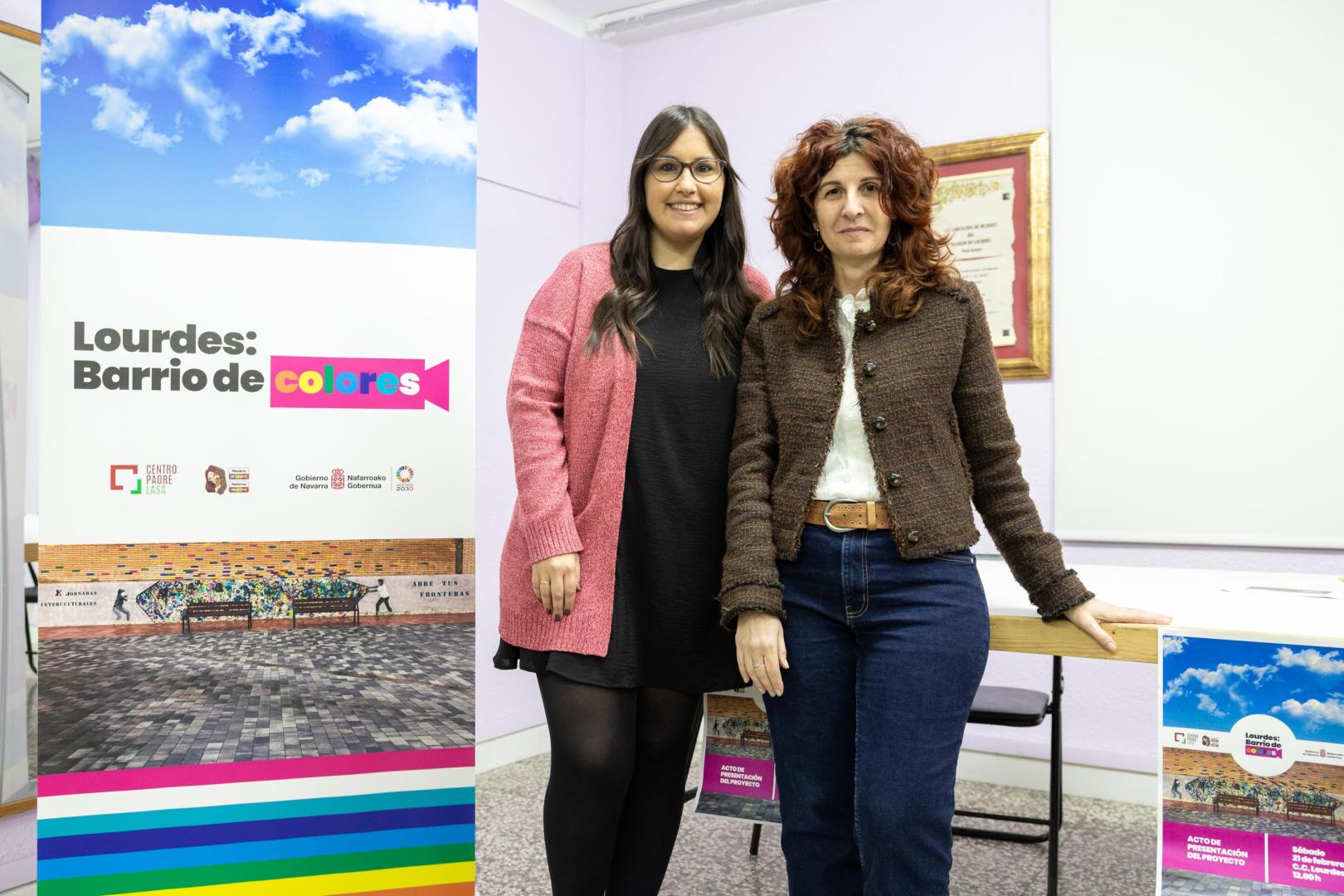 De izda. a dcha.: Claudia Hierro Rodríguez (responsable del Centro Lasa) y Eva Gurría Marco (directora de Políticas Migratorias del Gobierno de Navarra), con el cartel del proyecto ‘Lourdes: Barrio de Colores’