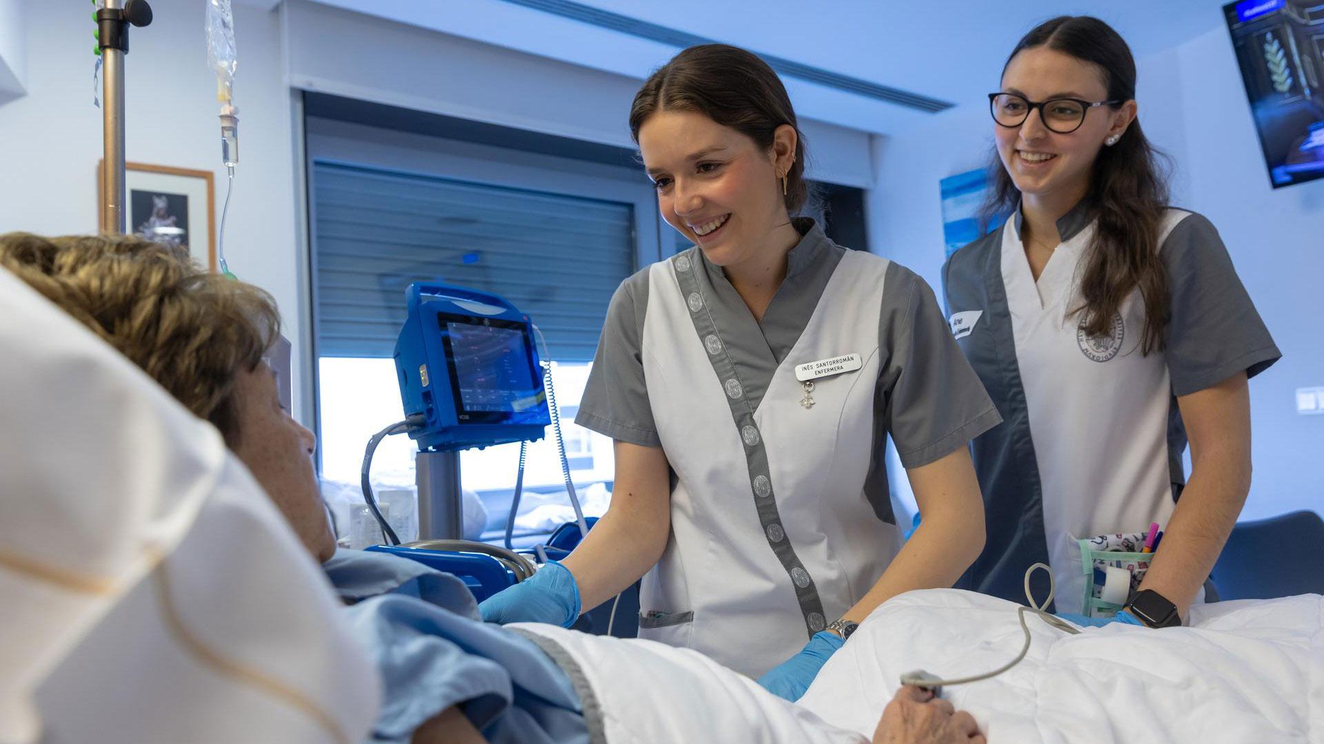 Una enfermera especializada, junto a una estudiante de Enfermería, atienden a una paciente hospitalizada en la planta de Oncología de la Clínica Universidad de Navarra