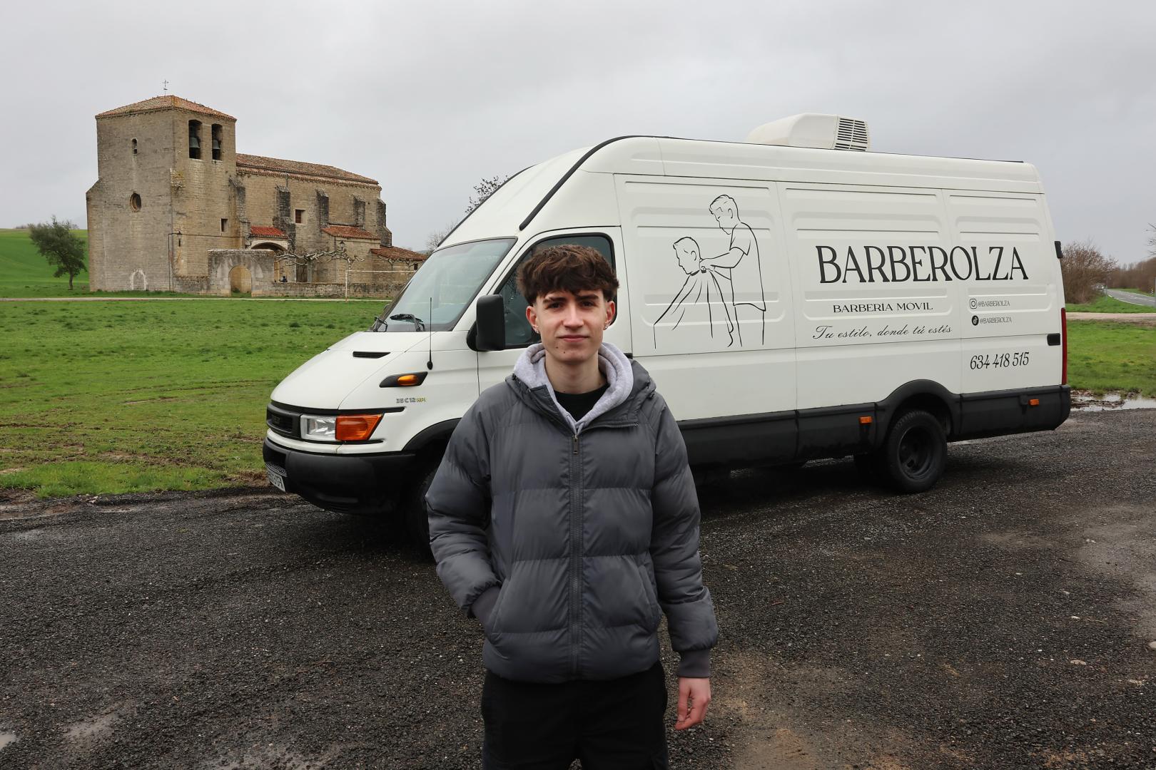 Ion Olza posa delante de la furgoneta ya rotulada y convertida en barbería móvil. Detrás la iglesia de su pueblo, Asiáin