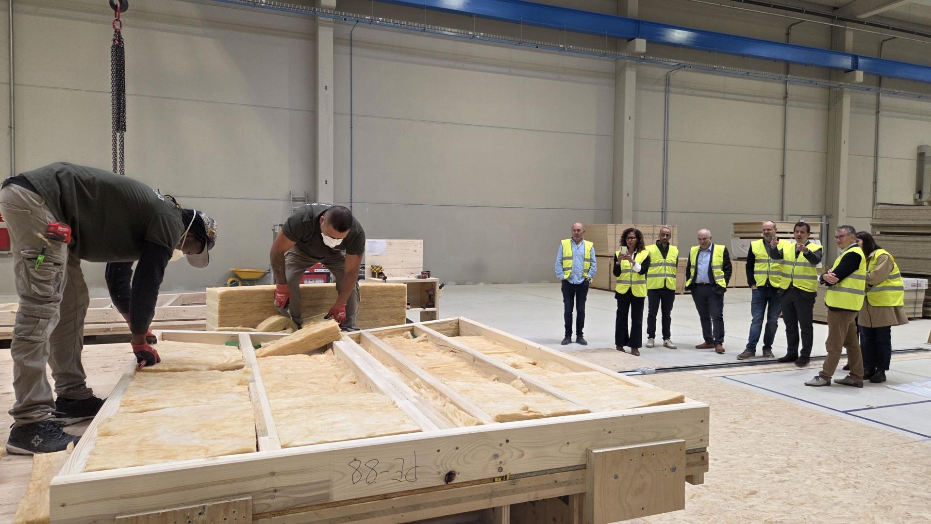 Dos operarios rellenan de material aislante un armazón de madera en la planta de Madergia de Aoiz durante la visita de las autoridades