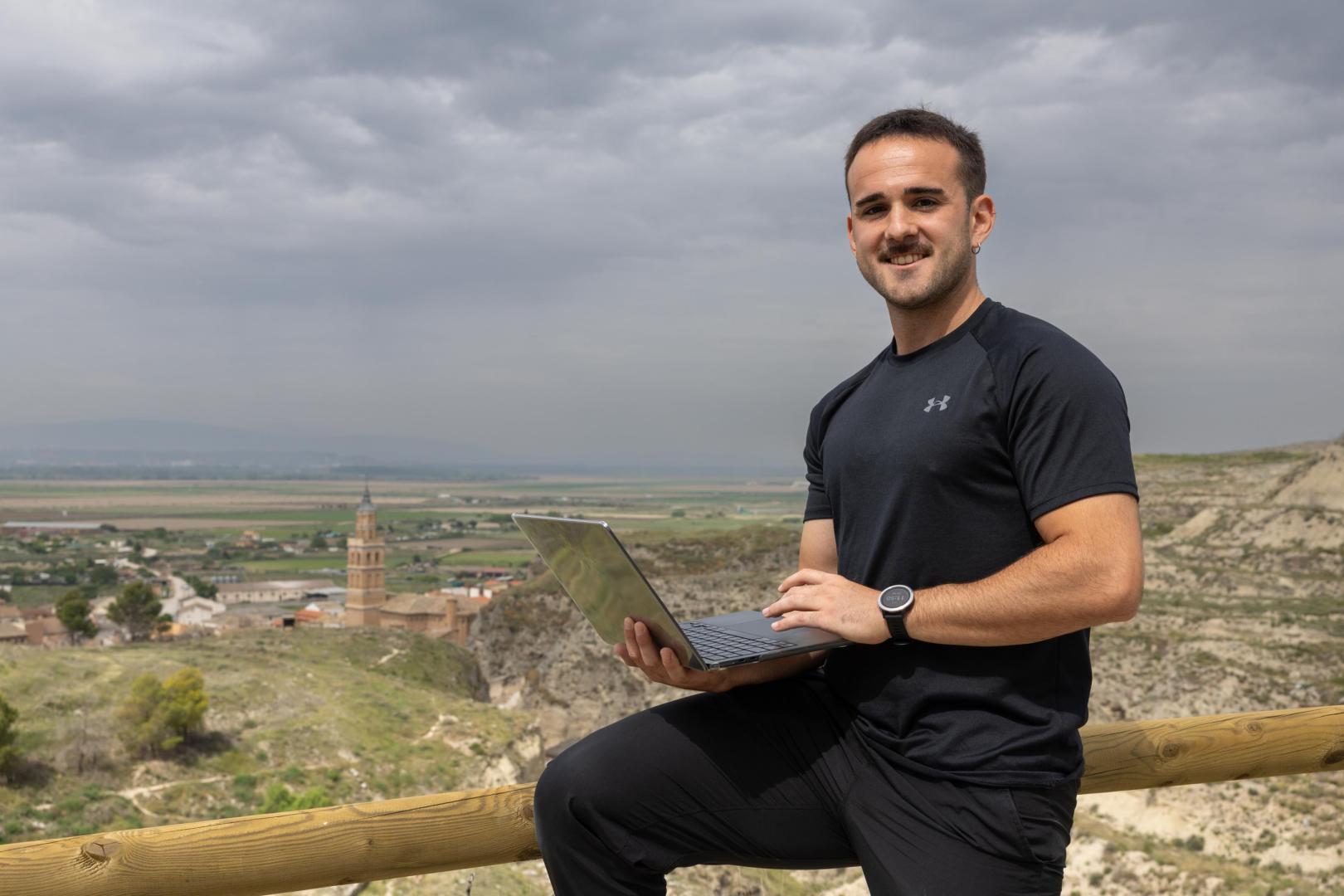 Alex Bienzobas Asensio, coach online, sujetando un portátil con Arguedas de fondo