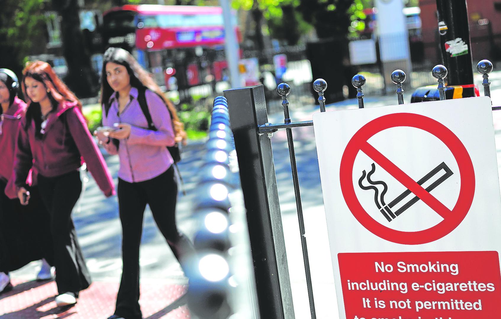 Jóvenes pasan junto a un cartel de ‘prohibido fumar’ frente a una estación de autobuses en el este de Londres