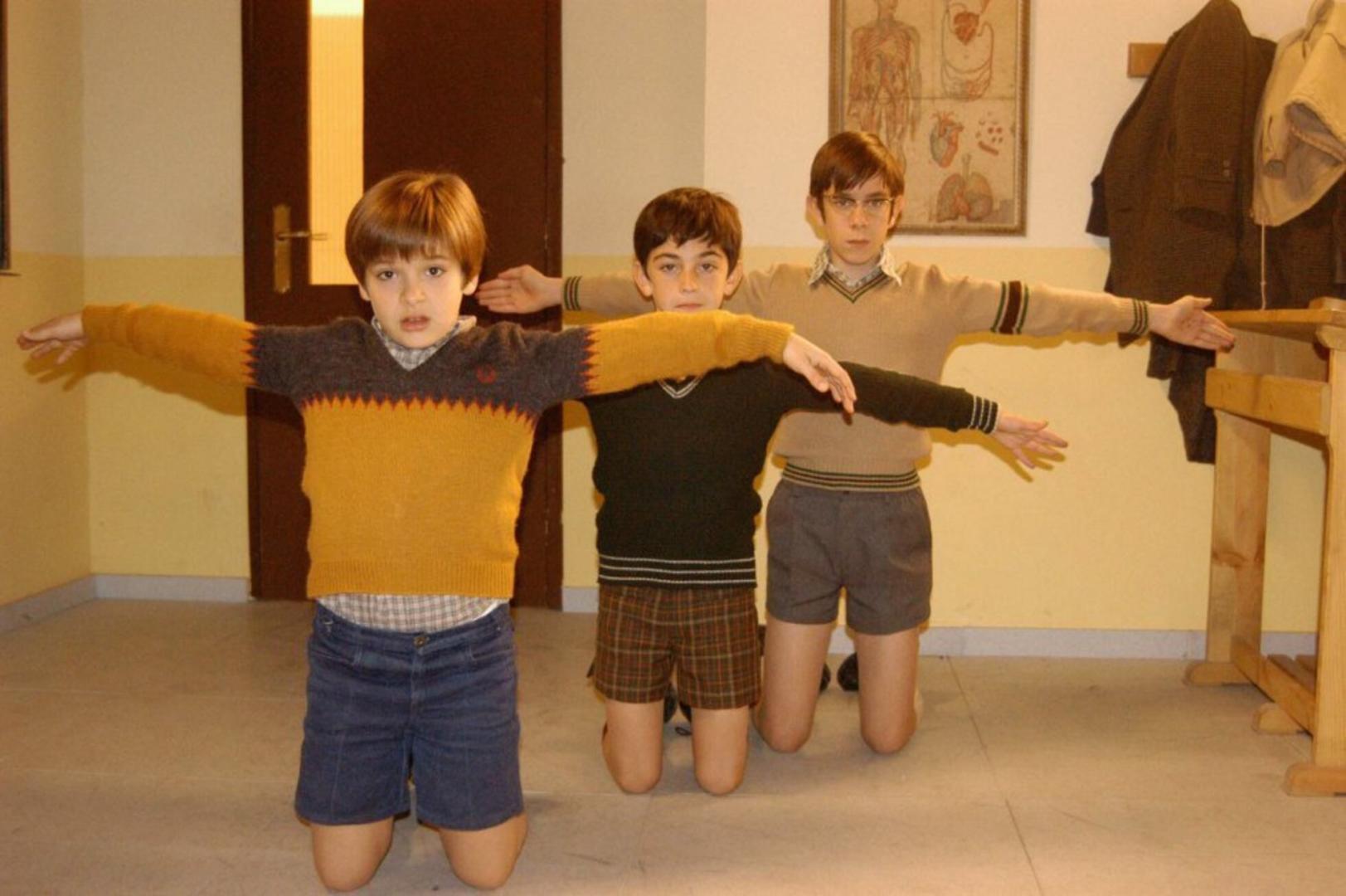 Carlos Alcántara (Ricardo Gómez) y sus amigos Josete (Santiago Crespo) y Luis (Manuel Dios), castigados de rodillas y con los brazos en cruz, en la serie 'Cuéntame cómo pasó' de TVE.