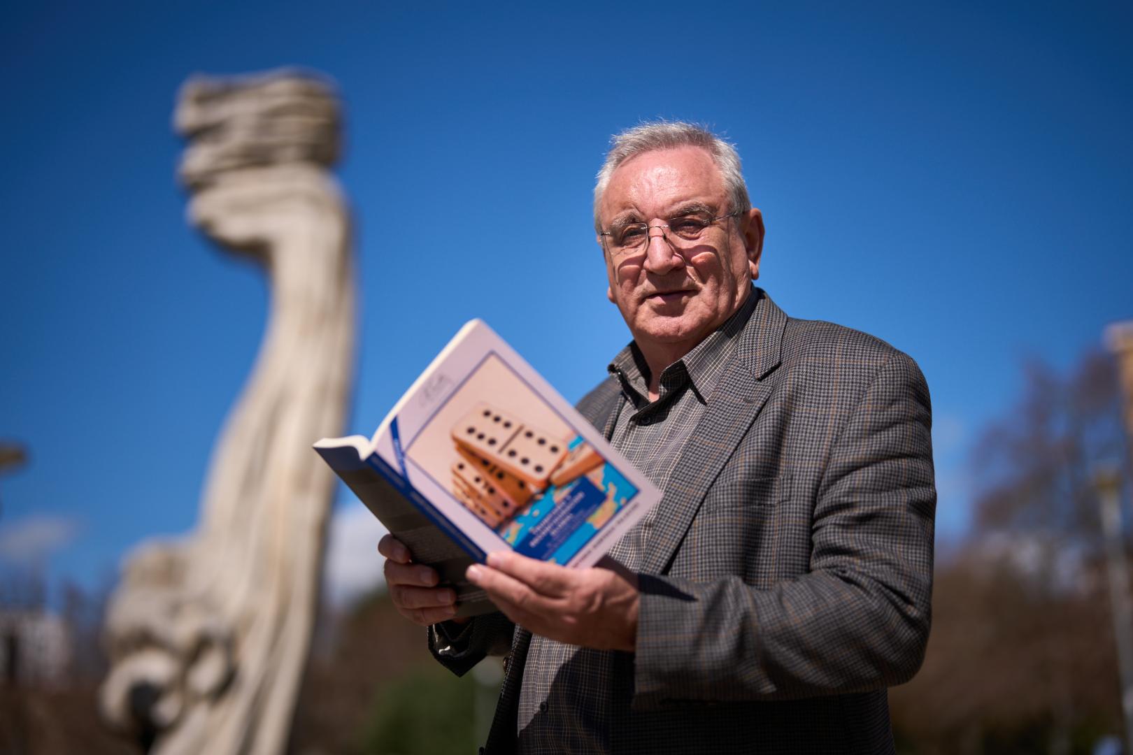 José A. Gurpegui posa con su libro en Pamplona delante de la escultura ‘Tramontana’, nombre que se da al viento frío y violento que sopla del norte o noroeste en el Mediterráneo occidental, y con el que se alude metafóricamente al cambio brusco que Trump está infringiendo al orden mundial.