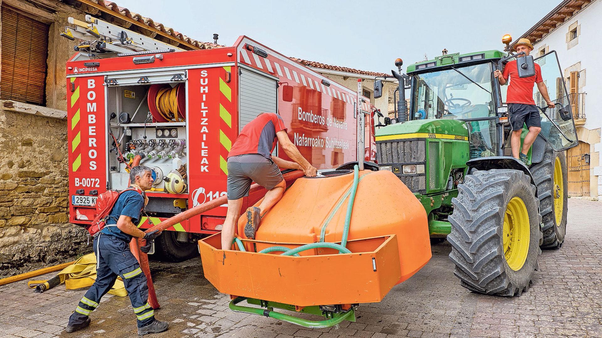 Un bombero ayuda a llenar de agua el depósito del tractor a dos vecinos en Orrio