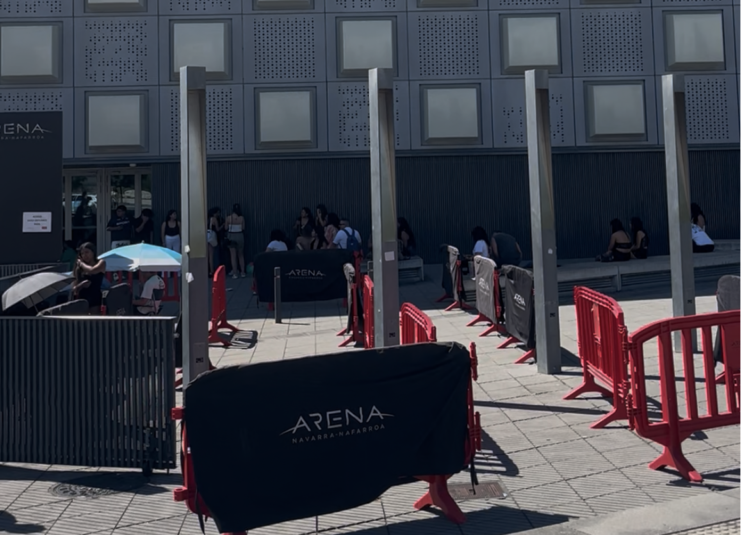 La gente esperando a que abran las puertas refugiándose del sol bajo paraguas y el porche del Navarra Arena