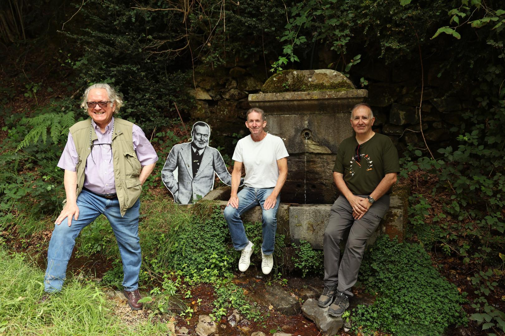 Desde la izquierda, Gerry Dawes, Tim Pinks y Miguel Izu, junto a la fotografía en cartón de Hemingway, colocada en la fuente donde el escritor dejaba a enfriar las botellas de vino, en la Fábrica de armas de Orbaizeta