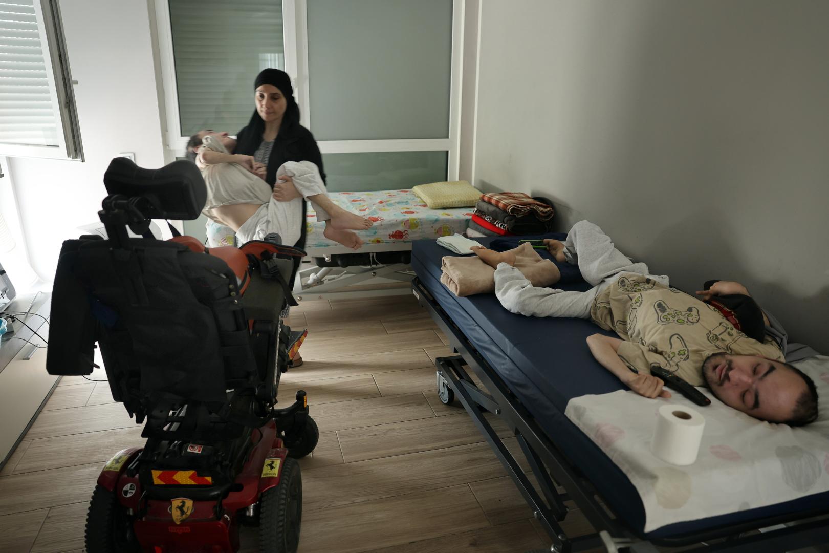Ha llegado el momento de salir a la calle. Latifa toma en brazos a sus dos hijos y los acomoda en sus respectivas sillas de ruedas eléctricas.