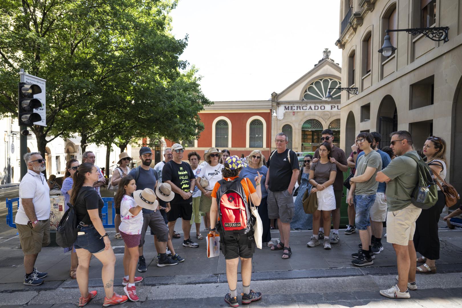 Un gran grupo de turistas, en el que se encuentran María Duran y Marc Paulet, atienden a la explicación de Laura Alonso, su guía, sobre la historia de la ciudad.