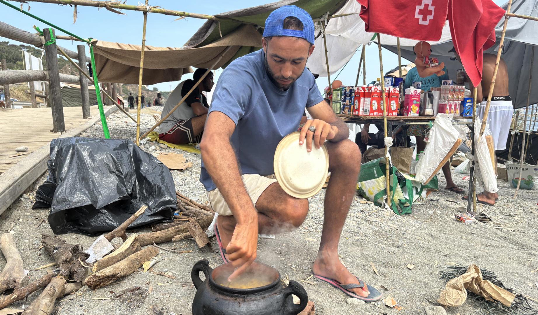 Varios inmigrantes se preparan la comida este miércoles en la playa del Trampolín