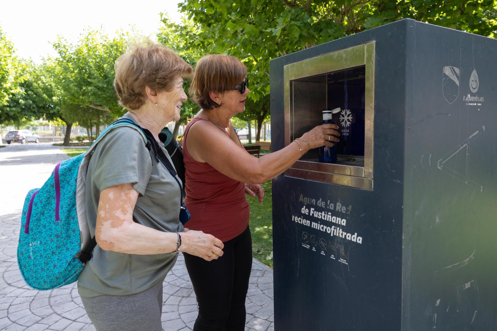 Dos mujeres rellenan una botella de agua en una de las fuentes instaladas en Fustiñana