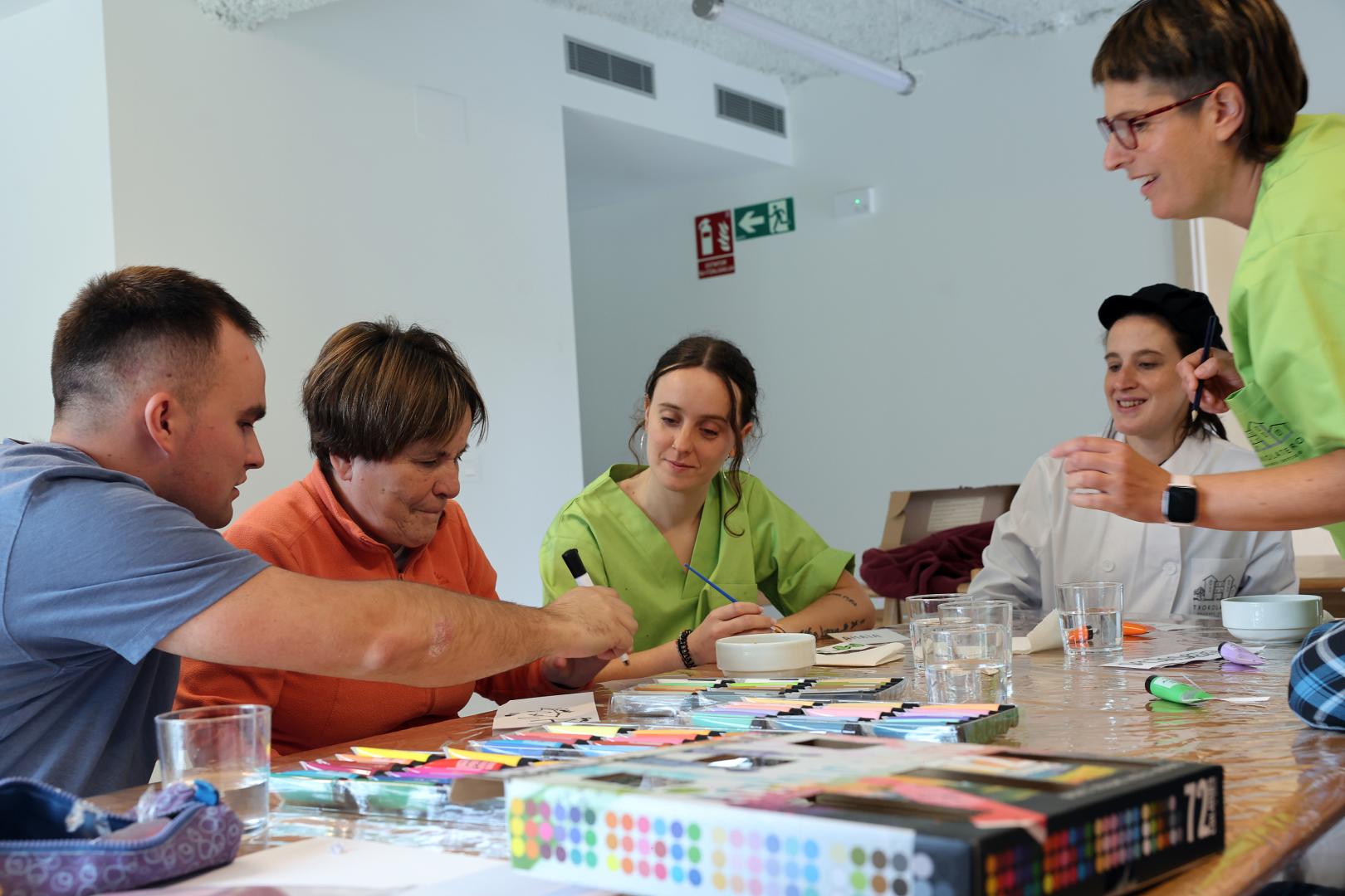 Xabier Carrascón Erice acompaña a su madre, María Josefa, en un ejercicio manual en presencia de la directora y trabajadora del Centro de Día ‘Txokolatero’, Amaia Lakarta Aizkorbe; la cocinera, Maitane Iribarren Ciáurriz; y la gerocultora, Marta Zubieta Ripalda.