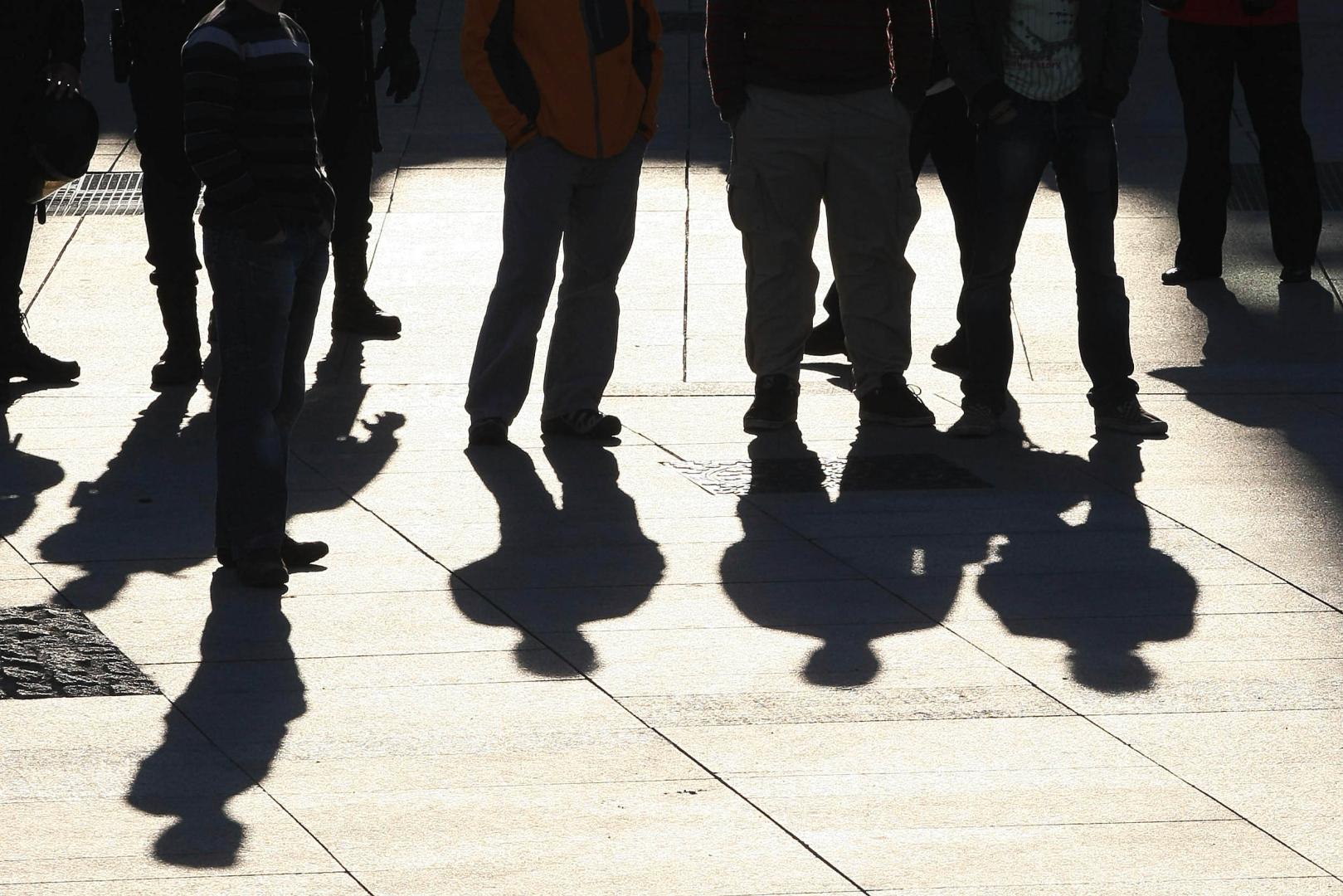 Un grupo de jóvenes reunidos en la calle, cuyas sombras se proyectan en el suelo