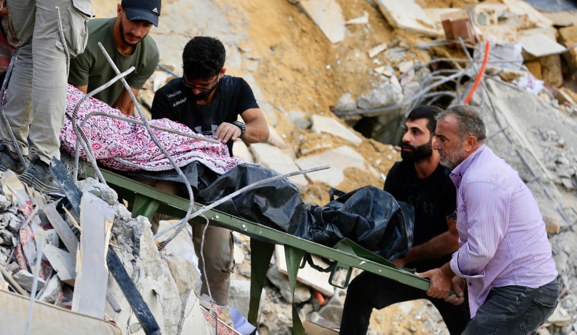 Varias personas transportan un cuerpo entre los escombros causados por un ataque aéreo israelí en Arab Salim