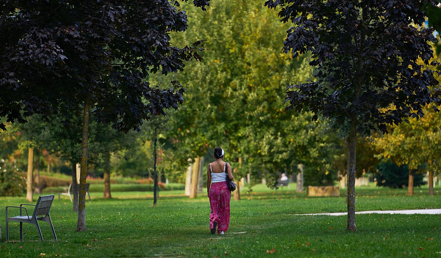 Una mujer pasea por una zona ajardinada de Pamplona
