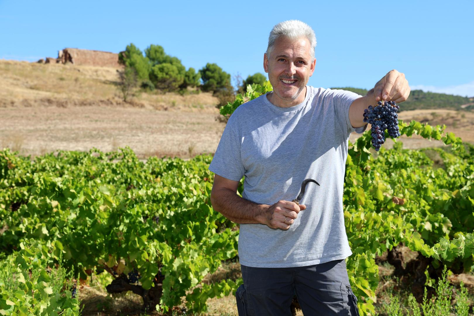 José Manuel Echeverría en el viñedo centenario del paraje de Yániz, con el corquete de su abuelo Nicolás. Al fondo la ermita de San Vicente