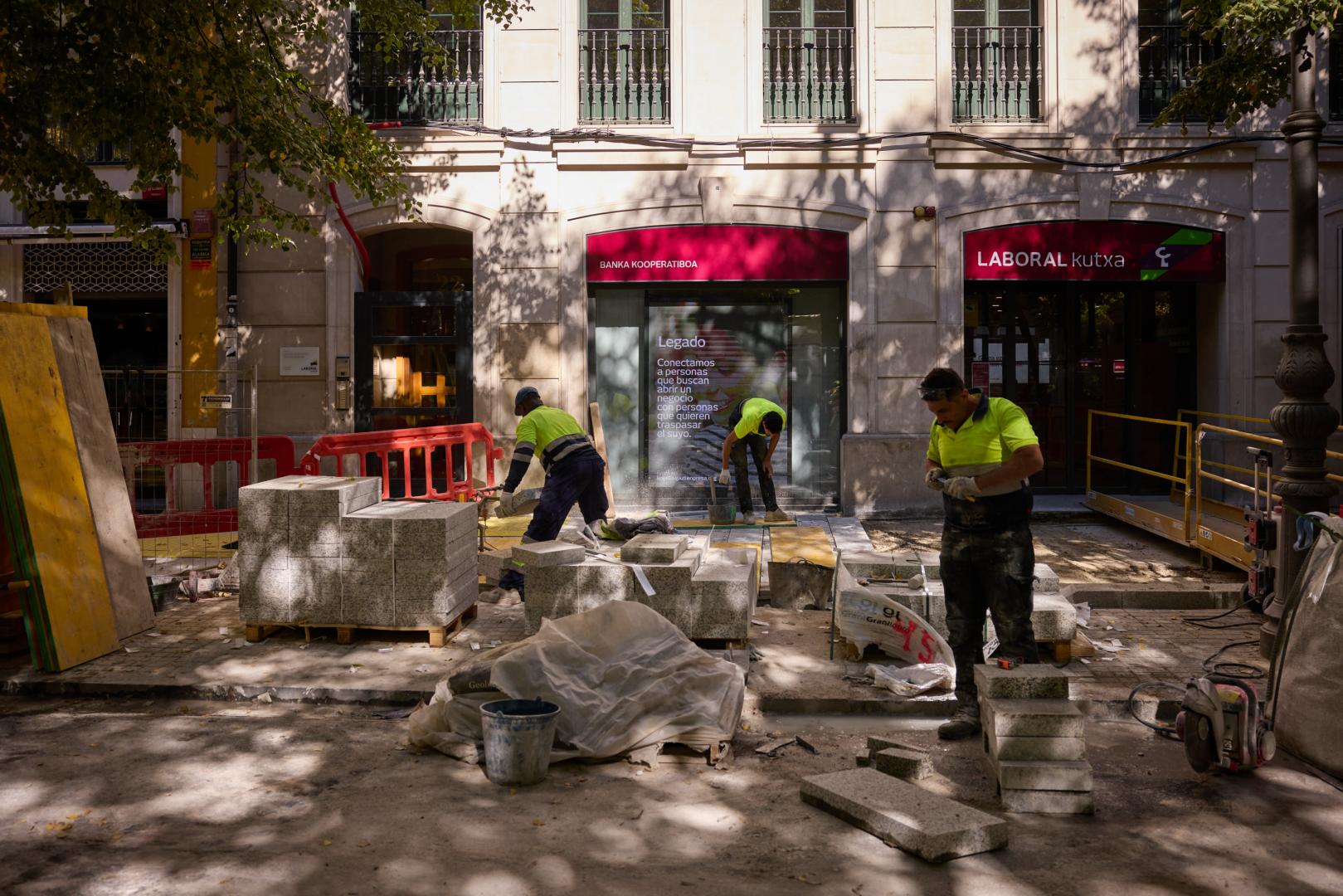 Tres operarios colocan las planchas de hormigón en la acera norte del paseo, junto a una sucursal bancaria y a un bar restaurante