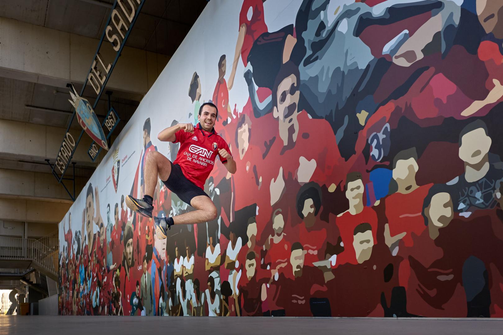 Mikel Recalde recrea el característico salto con el que cierra  sus vídeos frente al mural de Osasuna ubicado en el interior de El Sadar.