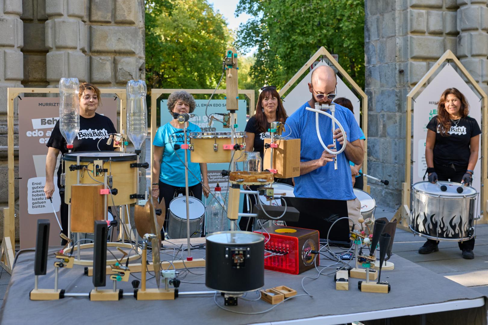 En primer plano, el lutier Jonathan García y su autómata musical elaborado con restos deresiduos de aparatos eléctricos y electrónicos. Detrás, componentes de la batucada BaraBatu.