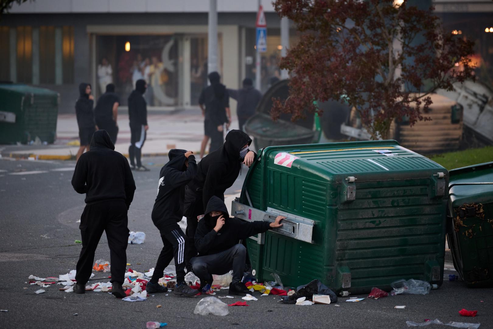 Cuatro manifestantes se protegen detrás de un contenedor volcado junto a la rotonda de la avenida Barañáin con calle Ermitagaña