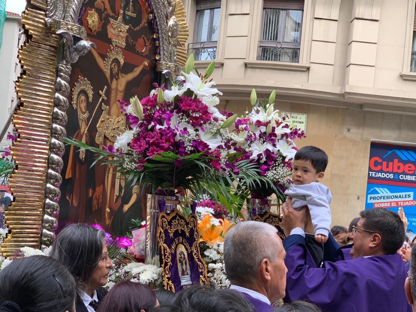 Un miembro de la hermandad acerca a un niño al Señor de los Milagros durante la procesión en la plaza de la Cruz de Pamplona